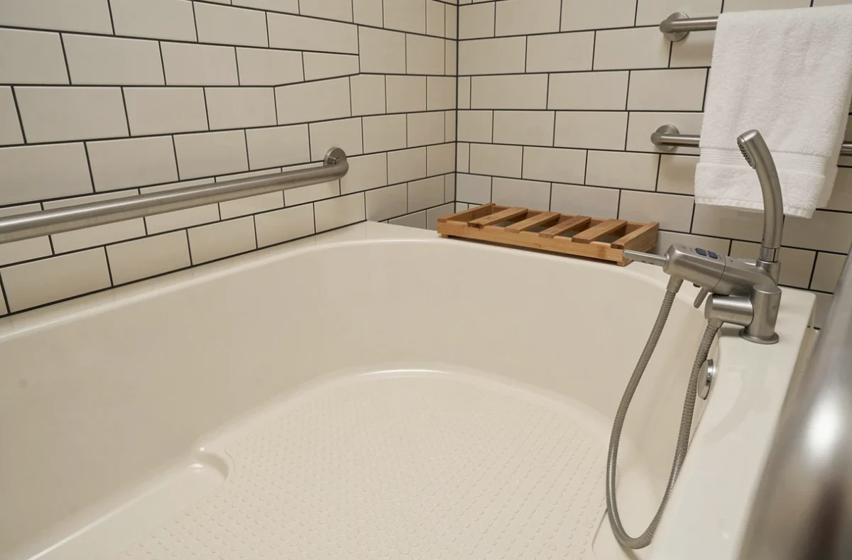 Détail intérieur d'une baignoire PMR avec siège intégré, surface antidérapante et barre d'appui en inox brossé dans une salle de bain adaptée
