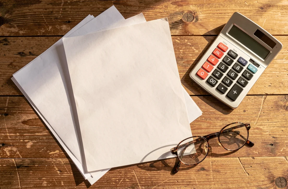 Documents de facturation, calculatrice et lunettes posés sur une table