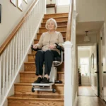 Femme âgée assise sur un monte escalier compact dans une maison individuelle avec escalier en bois